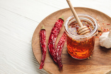 Plate with hot honey, garlic and dry chili peppers on light wooden background