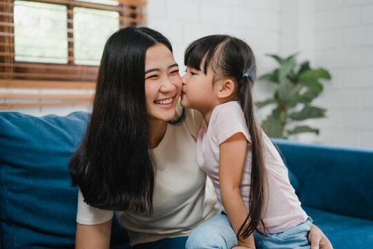 Happy Asian family mom and daughter embracing kissing on cheek congratulating with birthday at house. Self-isolation, stay at home, social distancing, quarantine for coronavirus prevention.
