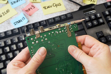 hands motherboard and keyboard near stickers about DevOps. DevOps Concept for software engineering...