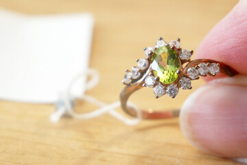 ring with peridot stone and diamonds in hands on wooden background
