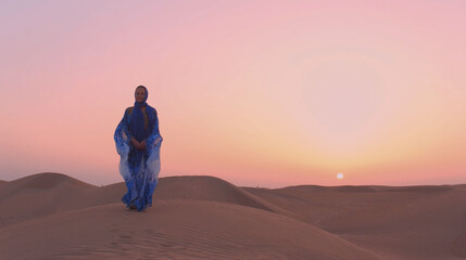 Fototapeta na wymiar Portrait of beautiful Arab woman weared in blue traditional dress in the desert during sunset.