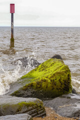 Seascape with metal groyne marker 38 and its associated granite breakwater rocks. Waves splashing over the wet stones. Choppy sea, with horizon. Portrait image with space for text. Horsey, Norfolk. UK - 440768383