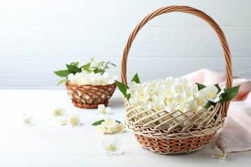 Fototapeta na wymiar Beautiful jasmine flowers in wicker basket on white wooden table. Space for text