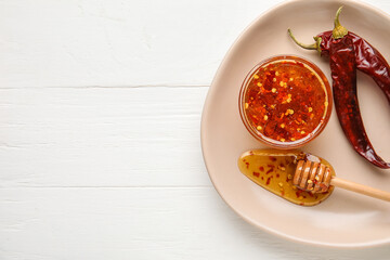 Plate with hot honey and chili peppers on light wooden background
