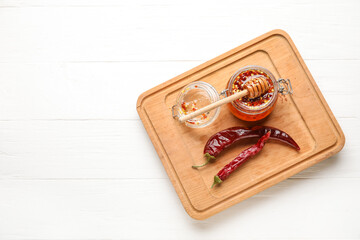 Fototapeta na wymiar Jar of hot honey and dry chili peppers on light wooden background