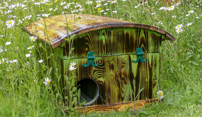 Bespoke hedgehog house made from recycled wood with domed roof, hinged for access. Resting in a natural wildflower garden with oxeye daisies and buttercups. Outdoor landscape image. Oxfordshire. UK. - 440768791