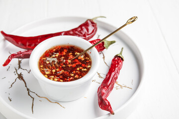 Tray with hot honey and dry chili peppers on light wooden background