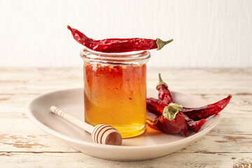 Jar of hot honey and dry chili peppers on light wooden background