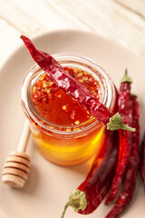 Jar of hot honey and dry chili peppers on light wooden background