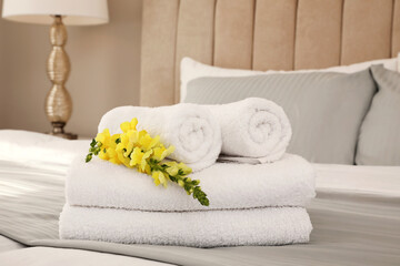 Fresh white towels with flower on bed indoors