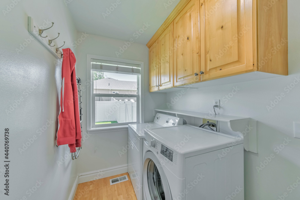 Wall mural Small white laundry room with wooden shelves, two washing machines and a window