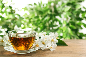 Glass cup of aromatic jasmine tea and fresh flowers on wooden table, space for text