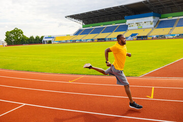 Fototapeta premium Joyful energetic African American sportsman athlete in yellow sportswear running at the stadium, preparing for competition, working hard to win the competitors