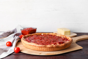 Board with tasty Chicago-style pizza, sauce and tomatoes on table