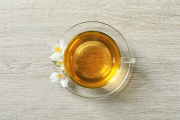 Glass cup of aromatic jasmine tea and fresh flowers on light wooden table, top view