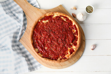 Board with tasty Chicago-style pizza, garlic and spices on light wooden background