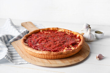 Board with tasty Chicago-style pizza, garlic and spices on light wooden background
