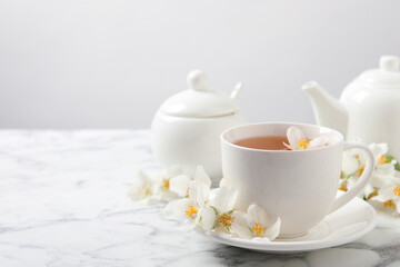 Aromatic jasmine tea and fresh flowers on white marble table, space for text