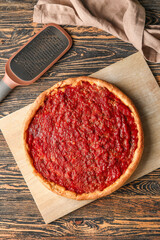 Board with tasty Chicago-style pizza and grater on wooden background