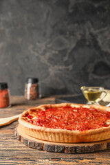 Board with tasty Chicago-style pizza and ingredients on wooden table