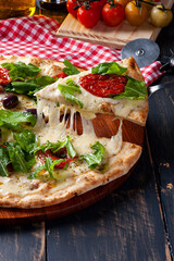 Brazilian-style pizza with mozzarella, sun-dried tomatoes and arugula. Someone taking a piece and stretching the cheese