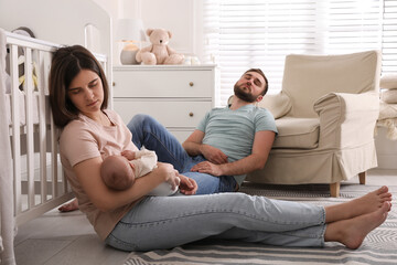 Tired young parents with their baby sleeping on floor in children's room - obrazy, fototapety, plakaty