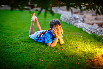 little boy in blue t-shirt lying on the grass  under tress
