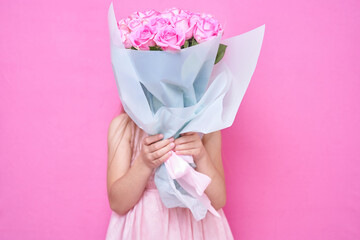 A little girl in pink dress with bouquet of roses, hid behind the flowers.The girl inhales the fragrance of flowers on pink backgraund