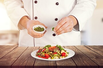 Chef dressing dish with fresh greens before it is going to be served for restaurant guests
