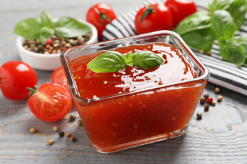 Spicy chili sauce with basil on grey wooden table, closeup