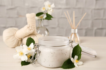 Jar of salt scrub and beautiful jasmine flowers on white wooden table
