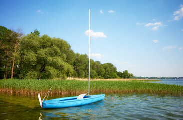 Small blue sailboat moored by reeds, Drawsko Lake, Poland.