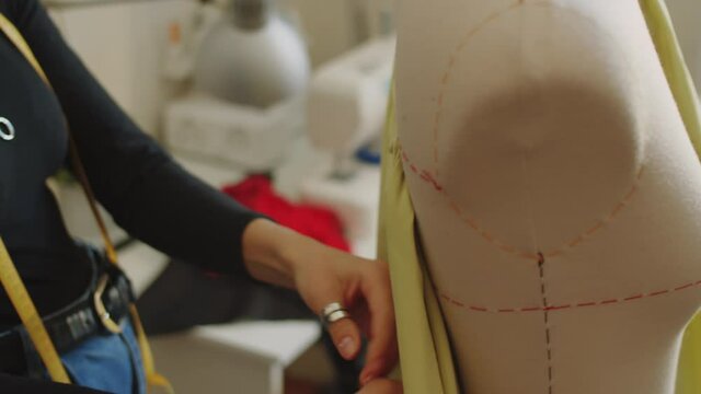 Female dressmaker using sewing pins while draping fabric on dress form in her workshop