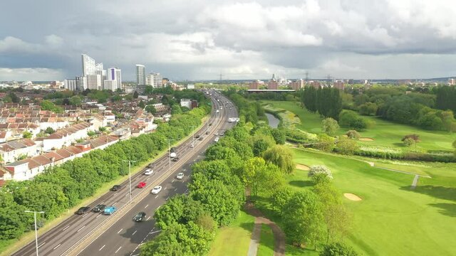 Multilane road leading around golf course, heading towards modern tall buildings.