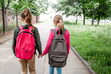 Back view Two schoolgirls going to school with backpacks. Back to school and friendship concept