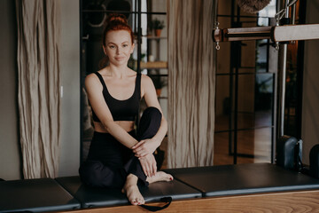 Beautiful young pilates trainer sitting with arms around legs in calm and relaxed position