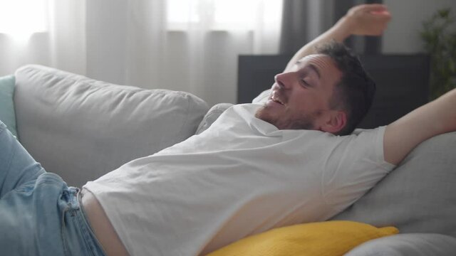 Happy relaxed young man rest lounge lean on couch enjoy peaceful mood, healthy lazy calm man dreaming breathing fresh air sit on comfortable sofa in living room on stress free cozy day at home