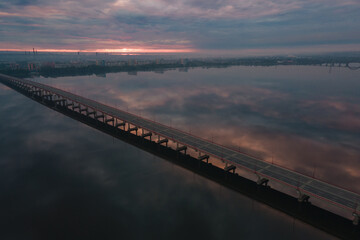 Fototapeta na wymiar Aerial drone filmed sunset, burning sky over the city and water, beautiful sunset or sunrise. Panoramic view over the bridge with the sun