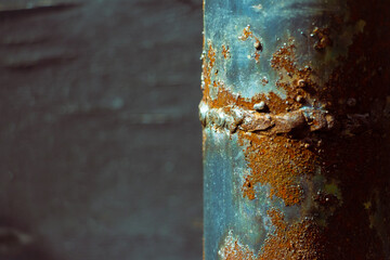 rusty metal pipe with weld seam on black wooden board background in dark tones with blue tint,...