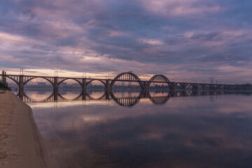 Bridge over the water during beautiful sunset and sunrise sun. Sunset over the bridge, purple blue yellow orange sky.