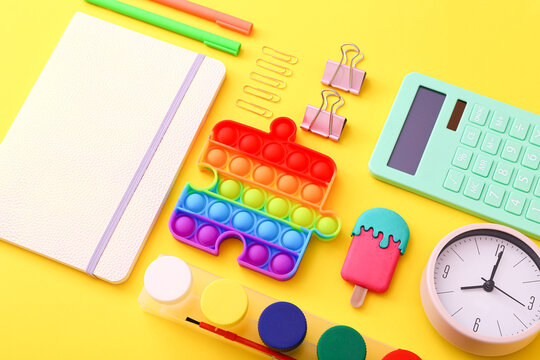 Close up of stationery, clock and silicone toy popit on yellow background