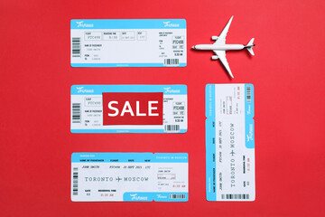 Flight tickets, plane model and SALE card on red background, flat lay