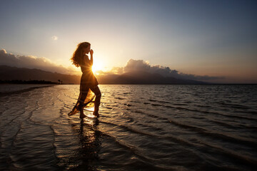 Fototapeta premium Beautiful woman dancing by the sea at sunset