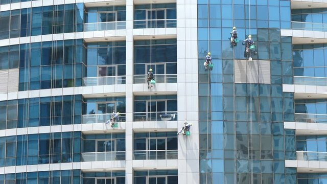 Window cleaners working, dangerous job, tall glass skyscraper building