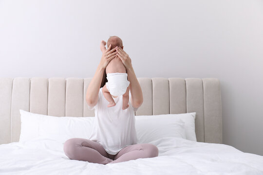 Mom holding her baby in diaper on bed at home