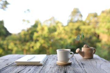 Notebook with white coffee cup and Stephania erecta Craib plant in watering can at outdoor