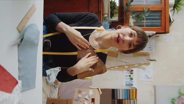Vertical footage of female dressmaker looking at camera and speaking about fabric while filming vlog in sewing studio