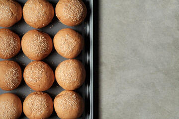 top view photograph shot with a half frame of many burger breads on the oven tray put on rusty kitchen table with empty copy space