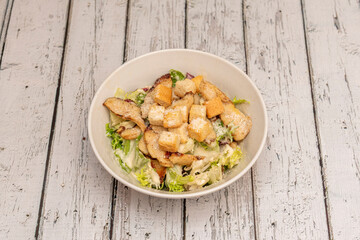 Popular Caesar salad recipe with croutons, breaded fried chicken pieces, lettuce, cheese and sauce in a white bowl