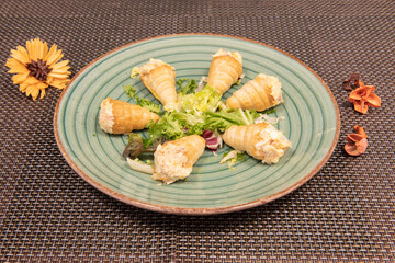 Puff pastry cones stuffed with Russian salad with mayonnaise and cooked potato on a green plate on a brown tablecloth